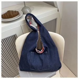 Détail du sac hobo en jean bleu avec poche avant et doublure florale vive sur une chaise