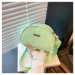Close-up of light green nylon crossbody bag with metal logo and woven strap detail
