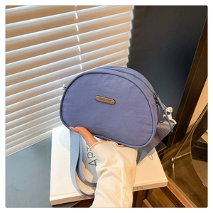 Detail of blue nylon crescent crossbody bag with metal logo and wide textile shoulder strap