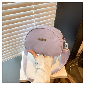 Detail of light purple nylon crossbody bag with metal logo plate and wide shoulder strap