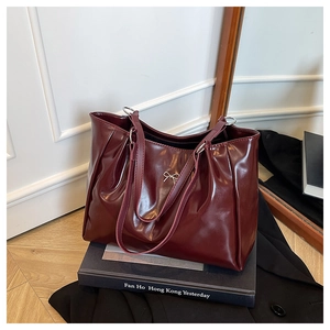 Detail of burgundy glossy tote bag featuring a gold bow accent on vintage books