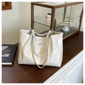 Detail of creamy white tote bag with silver metal bow and soft gathered faux leather texture
