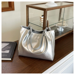 Close-up of a silver metallic tote bag featuring a decorative metal bow and soft texture
