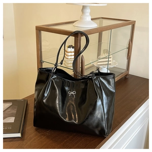 Detail of glossy black tote bag featuring a silver bow metal piece and sleek leather texture