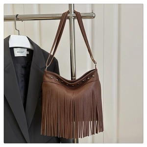 Detalle del bolso tote marrón oscuro con flecos y tachuelas metálicas en un perchero
