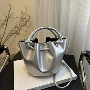 Chic silver metallic bucket bag with dual handles and shoulder strap on minimalist props