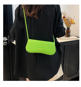 Close-up of lime green litchi leather crossbody bag with gold text on black outfit