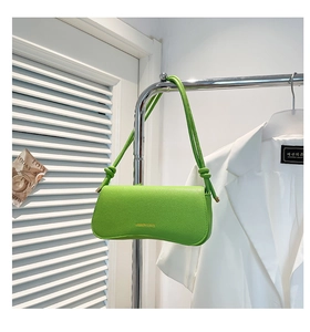 Detail of bright green pebble leather shoulder bag with golden text and knotted straps