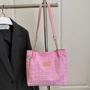 Pink checkered tote bag with gold chain strap hanging next to a dark blazer jacket