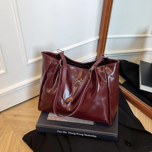 Glossy deep red tote bag with silver bow detail and slim straps in urban setting