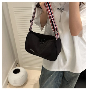 Détail d'un sac bandoulière en nylon noir avec large sangle rayée et fermeture éclair