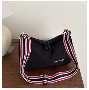 Détail du sac bandoulière en toile noire avec sangle rayée tricolore sur bois