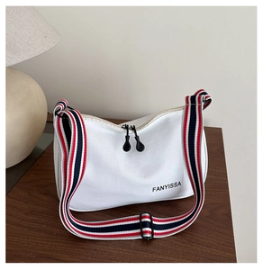 Détail du sac bandoulière en toile blanche avec sangle rayée et zips sur surface en bois