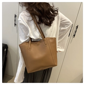 Close-up of brown leather tote bag with vertical stitching on white shirt background