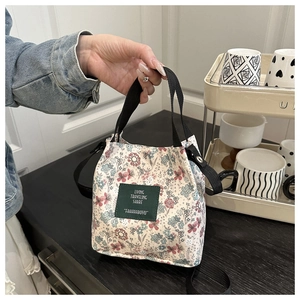 Detail of floral bucket bag featuring green label and black woven handles in a lifestyle setting
