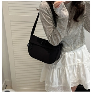 Detail of a black nylon crossbody bag with side white woven label on a model