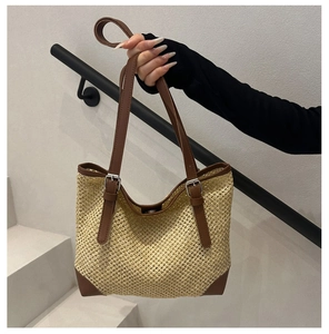 Close-up of woven straw tote bag featuring brown leather handles and silver metal buckles