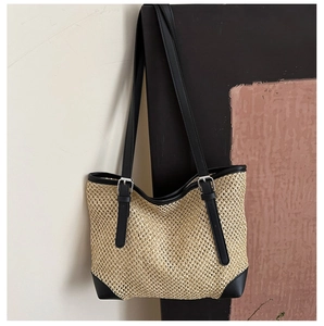 Detailed shot of woven straw tote bag featuring black leather trim and metal buckles