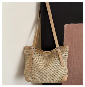 Close-up of woven straw tote bag featuring brown PU leather trim and metal buckles