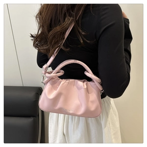 Détail d'un sac à bandoulière en cuir plissé rose clair porté par un mannequin en intérieur