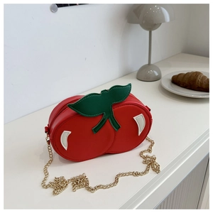 Detail of red cherry-shaped shoulder bag with green leaf accents and golden chain strap