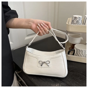 Detail of white crocodile pattern shoulder bag with a silver metal bow decoration