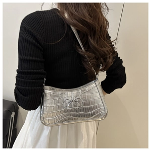 Detail of silver crocodile pattern shoulder bag with metallic bow and embossed texture