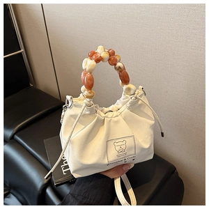 Detail of white pleated drawstring bag with amber marbled beaded handle and bear logo