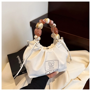 Detail of white drawstring handbag featuring a beaded handle with amber and ivory beads