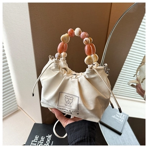 Detailed view of white drawstring bag featuring colorful beaded handle and bear brand label