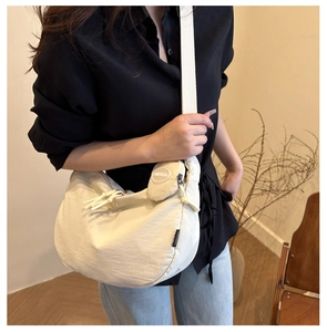 Detail of a beige crescent crossbody bag with a round coin purse on a wide shoulder strap