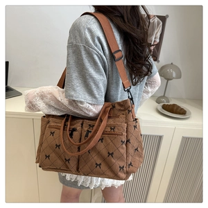 Close-up of brown corduroy shoulder bag featuring bow prints and multi-zipper pockets