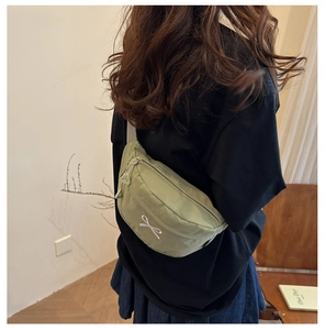 Detail of light green canvas crossbody bag with white bow embroidery on a model