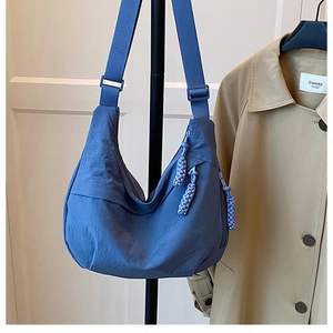 Close-up of a deep blue hobo crossbody bag with a distinctive braided zipper pull detail