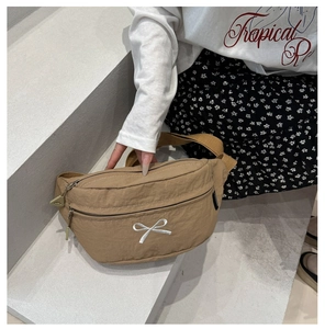 Detail of khaki nylon chest bag featuring white bow embroidery and double zippers