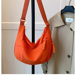 Detail of orange crescent crossbody bag with braided rope charms and nylon texture