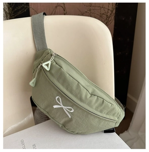Detail of light green chest bag with bow embroidery hanging on a white chair