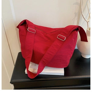 Detail of red crossbody tote bag featuring wide strap and silver metal buckle