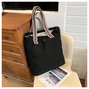 Detail of black canvas tote bag showing striped webbing handles and metal logo ornament
