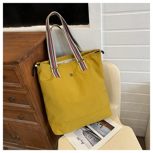 Detail of ginger yellow canvas tote bag featuring a colorful striped shoulder strap