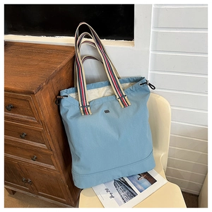 Detail of light blue tote bag with striped handles and drawstring closure on a chair