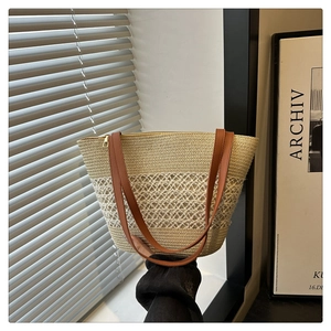 Detail einer handgehaltenen Stroh-Eimertasche mit braunen Lederriemen und Reißverschluss