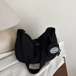 Minimalist black nylon crescent shoulder bag with a round mini pouch on a stylish wooden desk