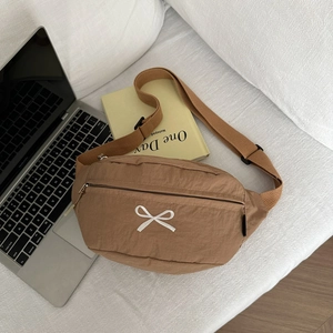 Brown nylon crossbody bag with embroidered white bow on a desk with a laptop
