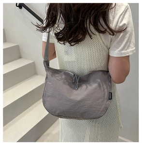 Detail of grey half-moon nylon crossbody bag with drawstring zipper and brand label