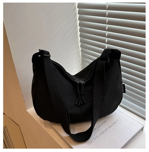 Detail of a black hobo bag showing the woven shoulder strap and tassel zipper pull