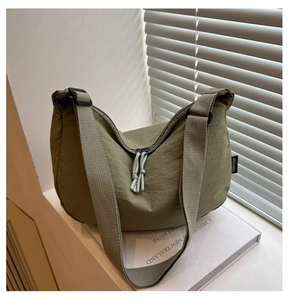 Detail of dark green nylon crescent bag featuring adjustable strap and side brand label