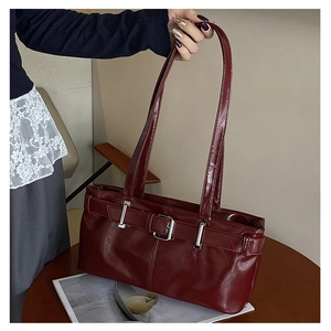 Detail of burgundy glossy leather baguette bag with silver buckle and sleek shoulder straps