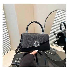 Detail of glittery flap and silver heart-shaped twist lock on black crossbody bag