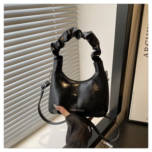 Close-up of a black glossy cloud handbag featuring a unique ruched scrunchie handle
